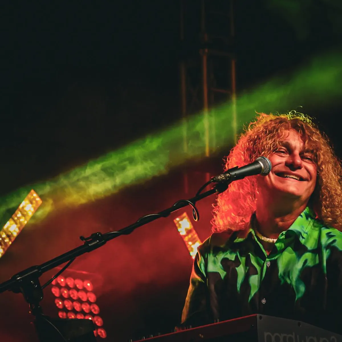 The keyboard player singing under green and red stage light