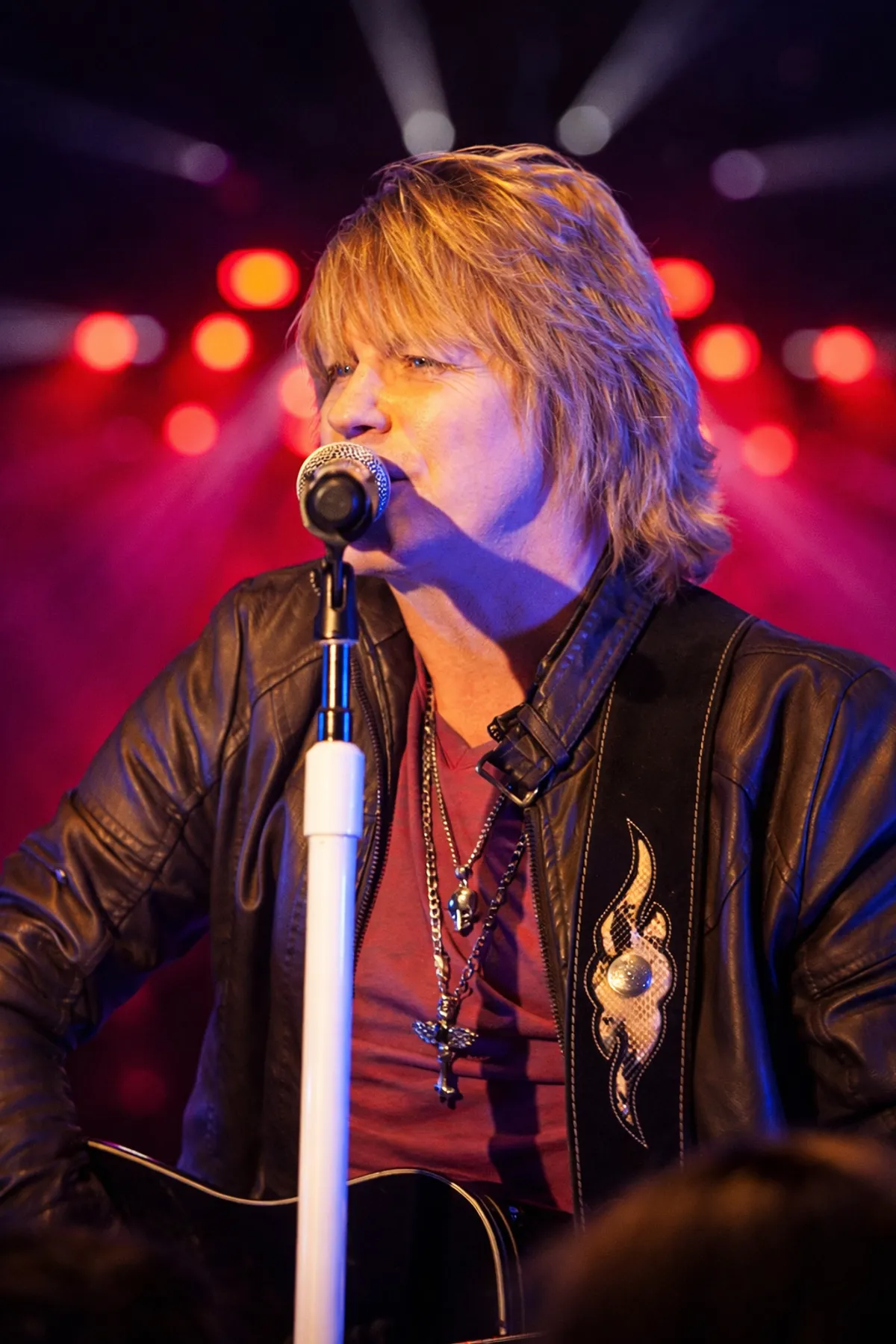 Doug Shepard singing at the mic in a leather jacket, red and purple lighting