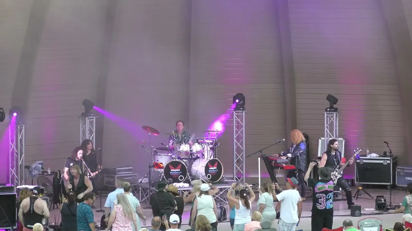The Stubbs Park crowd on their feet with phones raised as the band plays under purple light