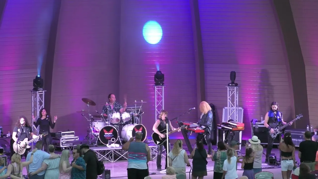 Crush on the Stubbs Park bandshell stage after dark, the band lit in purple and blue with the crowd standing at the front