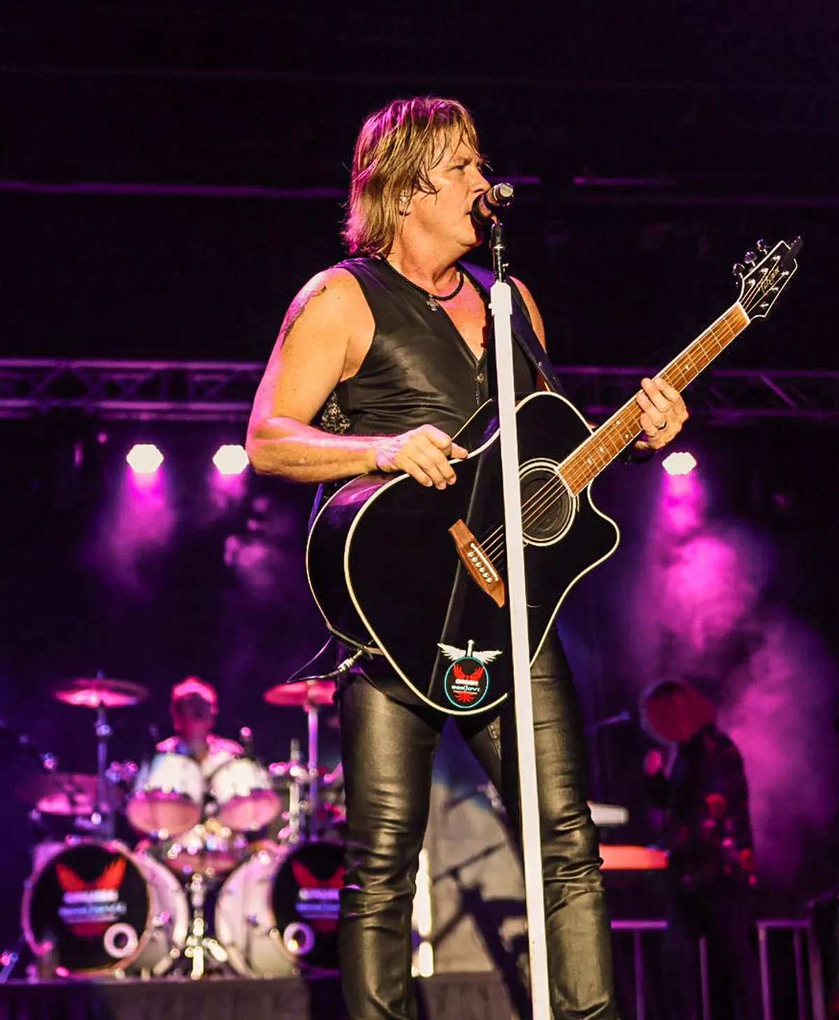 Doug Shepard with an acoustic guitar under magenta stage light