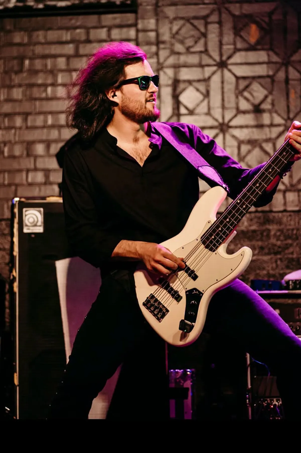 The bass player in sunglasses under purple stage light
