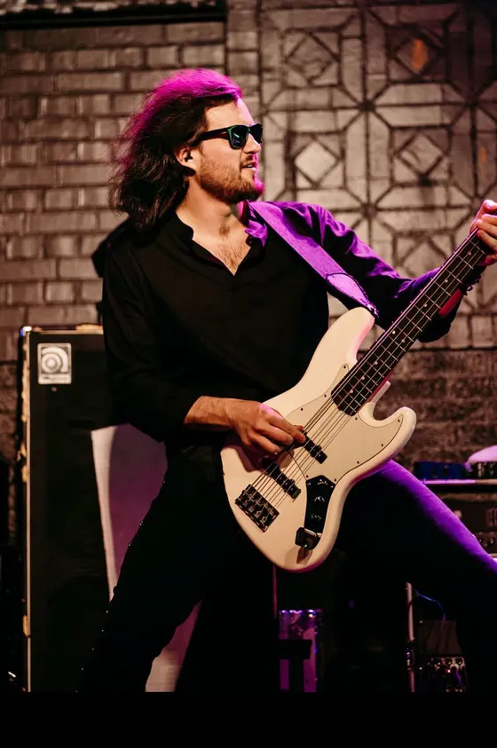 Jeff Smith in sunglasses playing a white jazz bass in front of an Ampeg cabinet