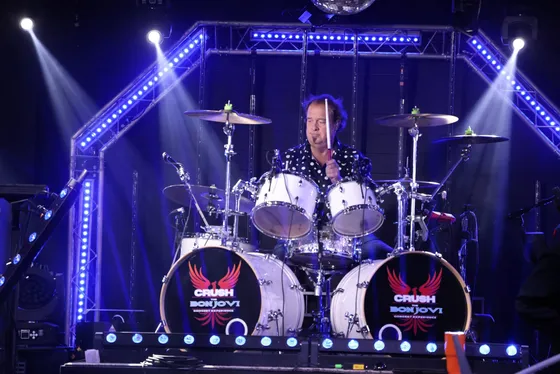 Todd Green behind a white kit with Crush logo bass drum heads, blue LED truss above him